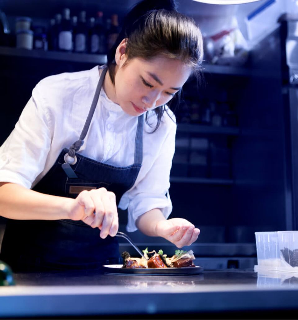 A woman working on a fancy dish in a restaurant kitchen
